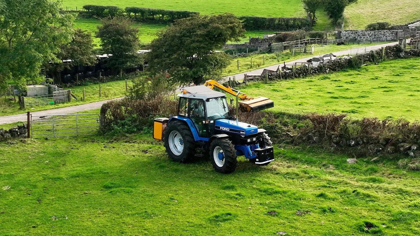 Traktor mit Anbaugerät auf einer grünen Wiese im Sonnenschein