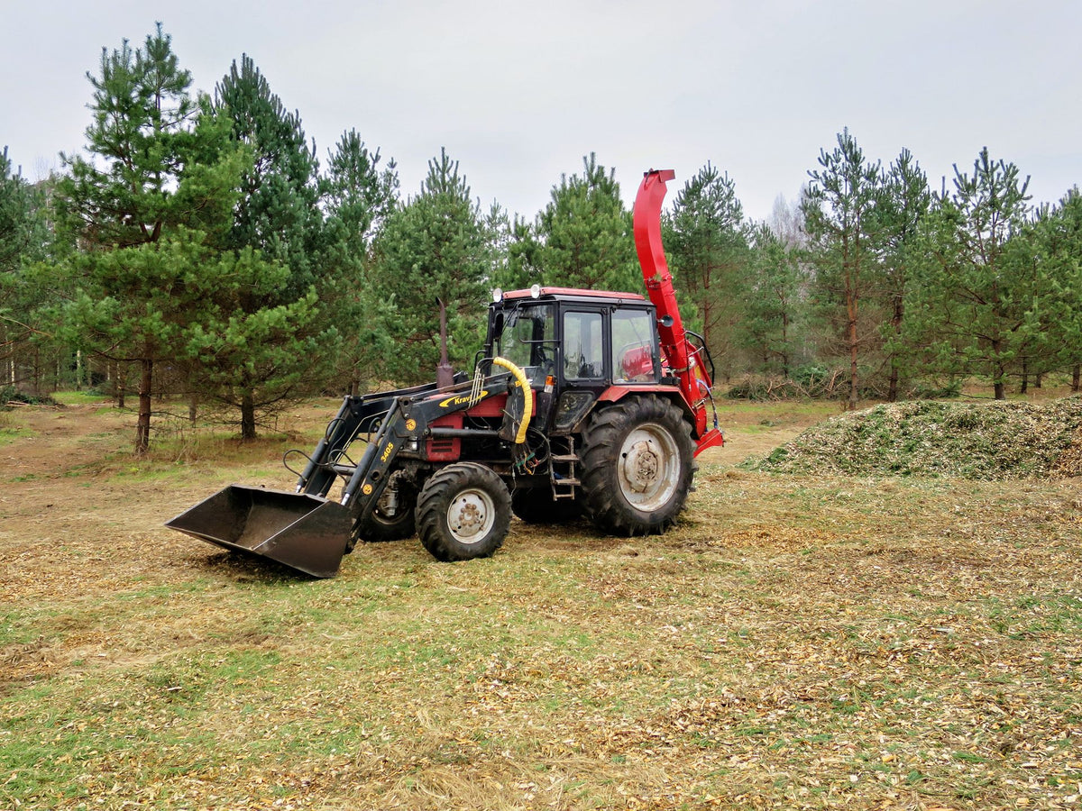 Rode trekker met hakselaar aan het werk in een bos