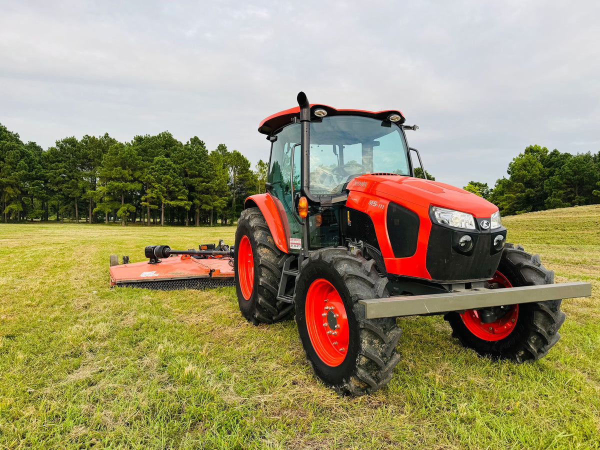 Rode trekker met klepelmaaier op een groen perceel met bomen op de achtergrond