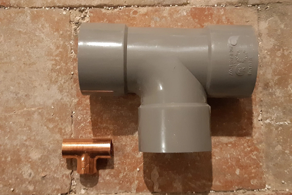 Grijs PVC T-stuk naast een koperen T-stuk